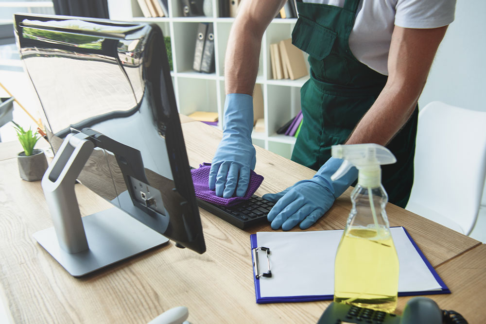 Person cleaning keyboard and computer in office